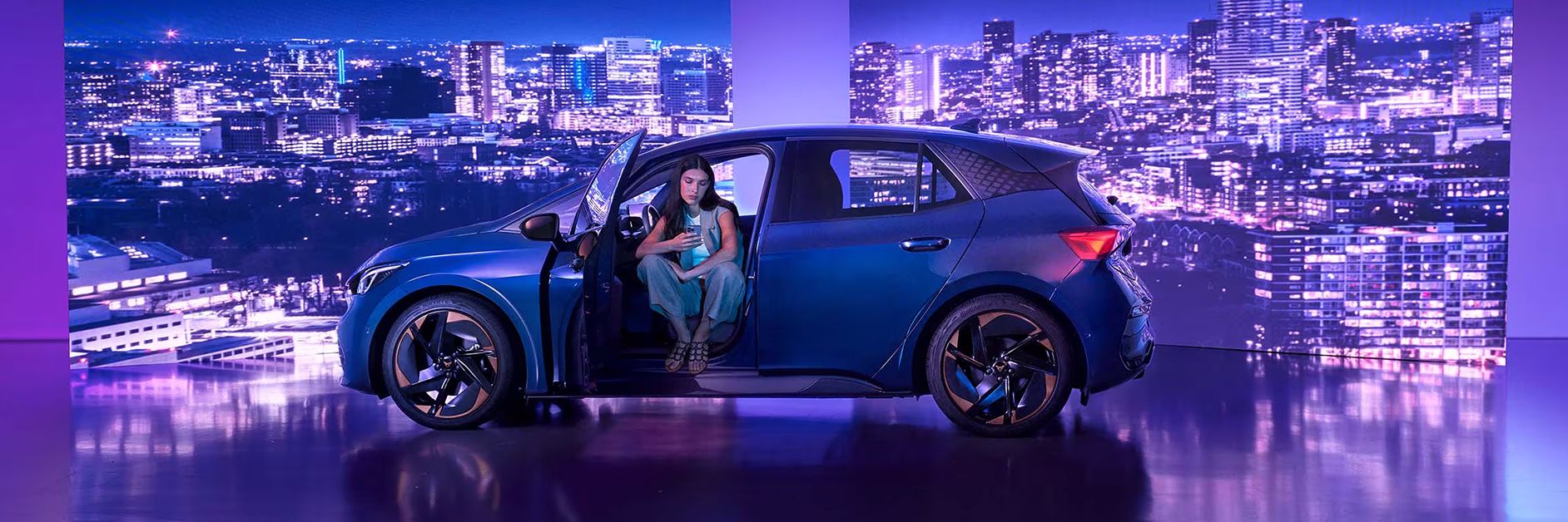 A lady sitting in an Aurora blue CUPRA Born while checking her phone