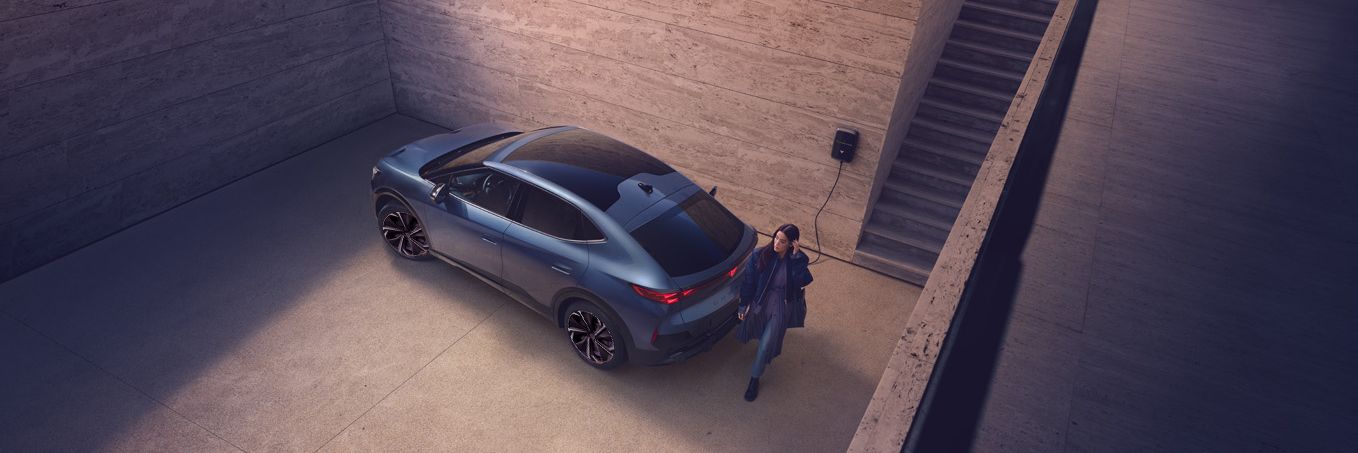 A girl walking behind CUPRA Tavascan and the car is charging 