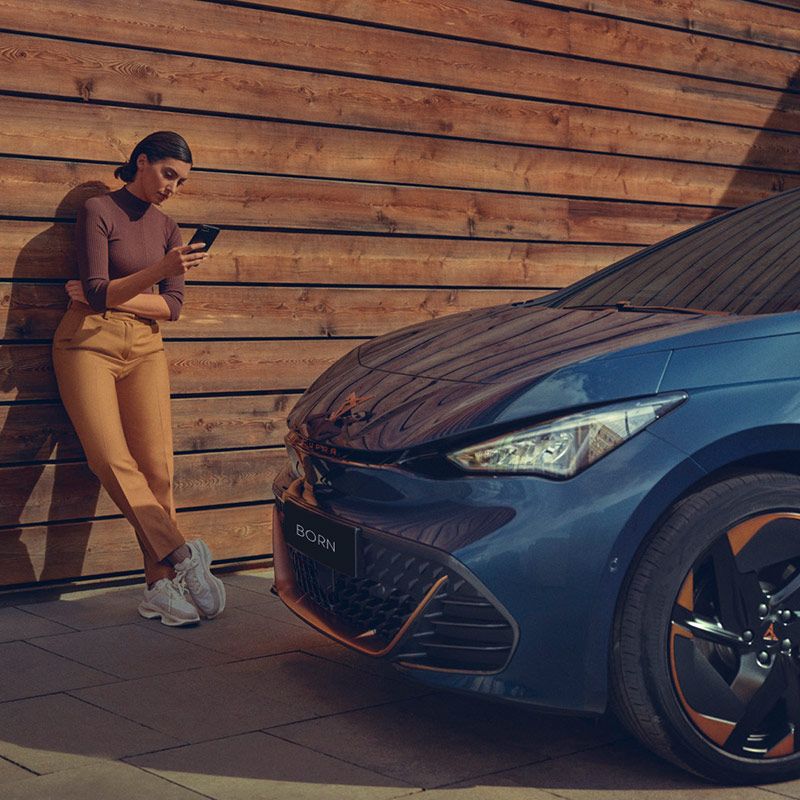 A lady checking her phone beside a CUPRA Born