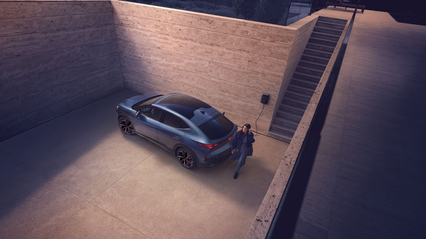 A girl walking behind CUPRA Tavascan and the car is charging 