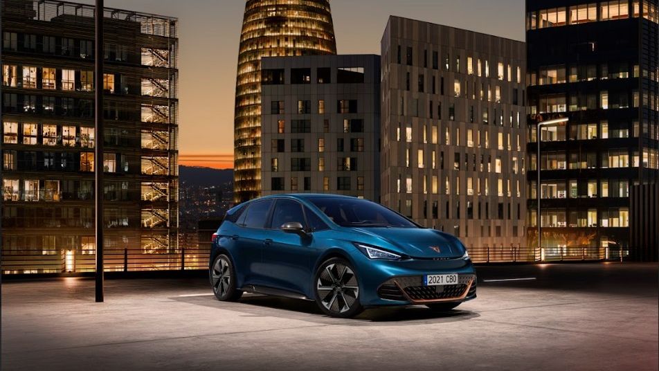 CUPRA Born parked by a parking lot with a city sunset view behind