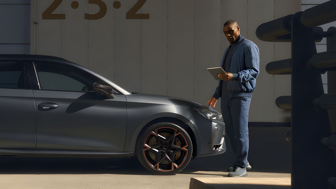 Side view of the CUPRA Leon while a service man is checking on his tablet about the car