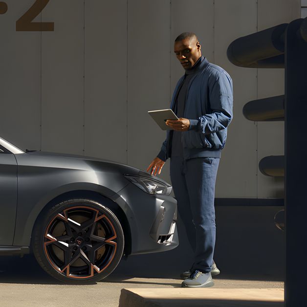 Side view of the CUPRA Leon while a service man is checking on his tablet about the car