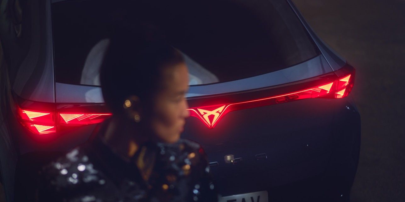 Close up shot of a woman standing behind of CUPRA Tavascan, rear light is lighting up