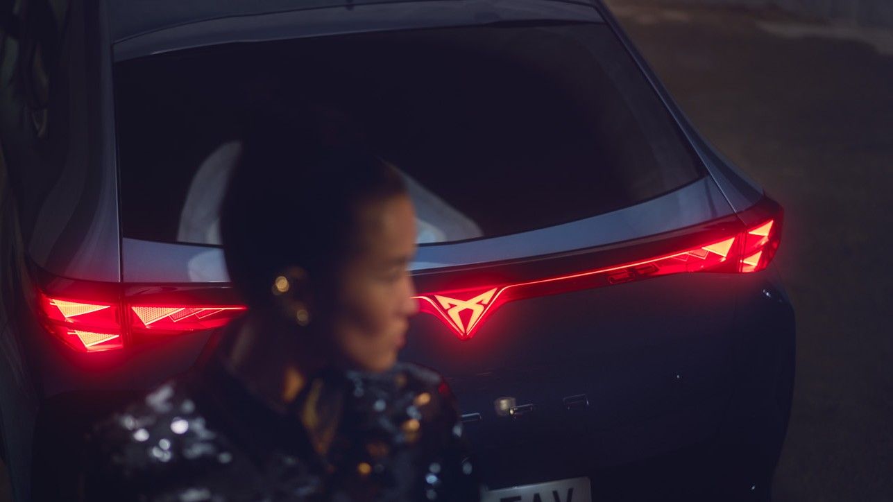 Close up shot of a woman standing behind of CUPRA Tavascan, rear light is lighting up