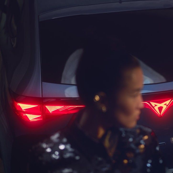 Close up shot of a woman standing behind of CUPRA Tavascan, rear light is lighting up