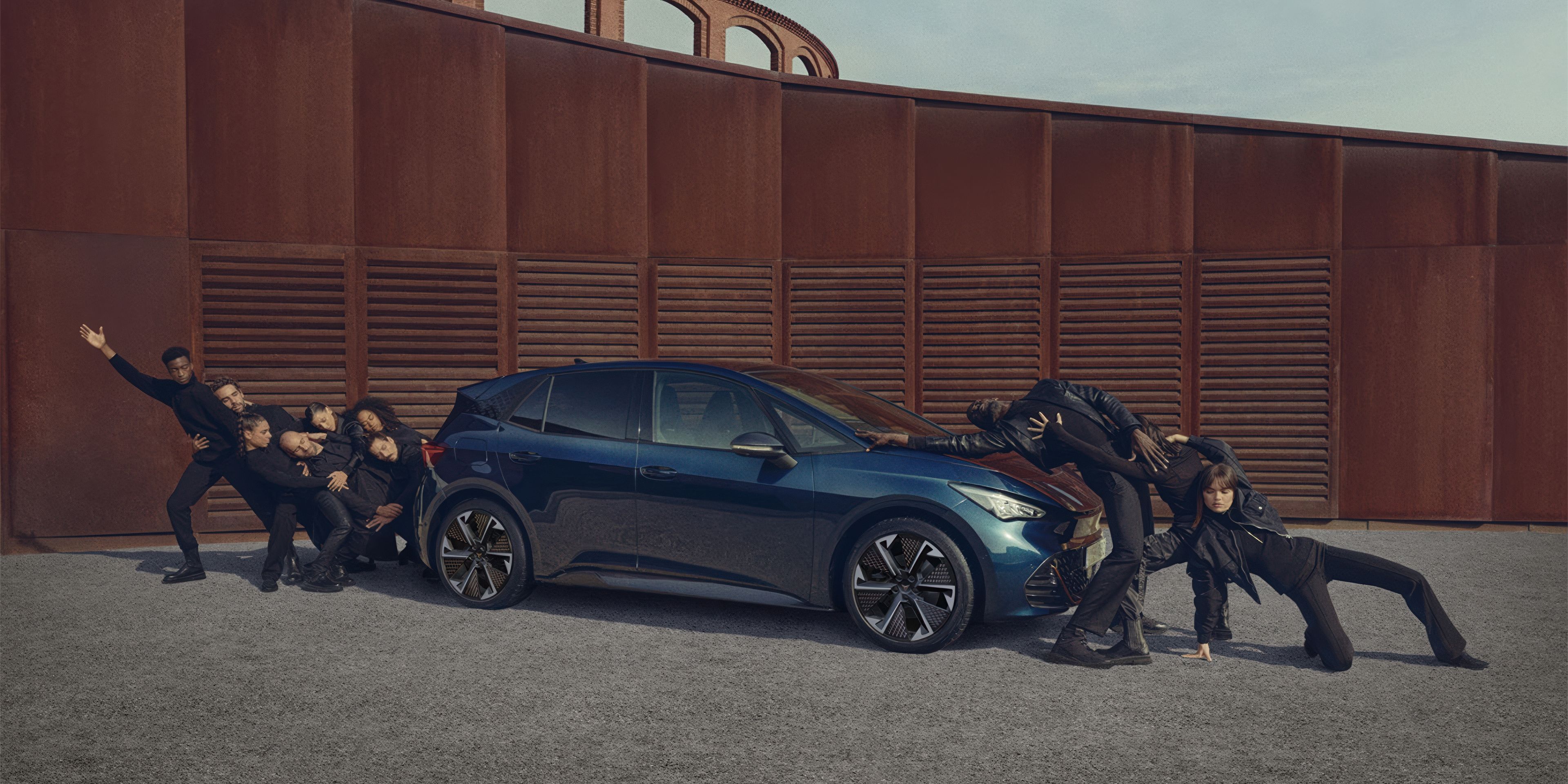 CUPRA Born in Aurora Bklue with 20 inch Thunderstrom aero rims with people posing infront and behind the car.