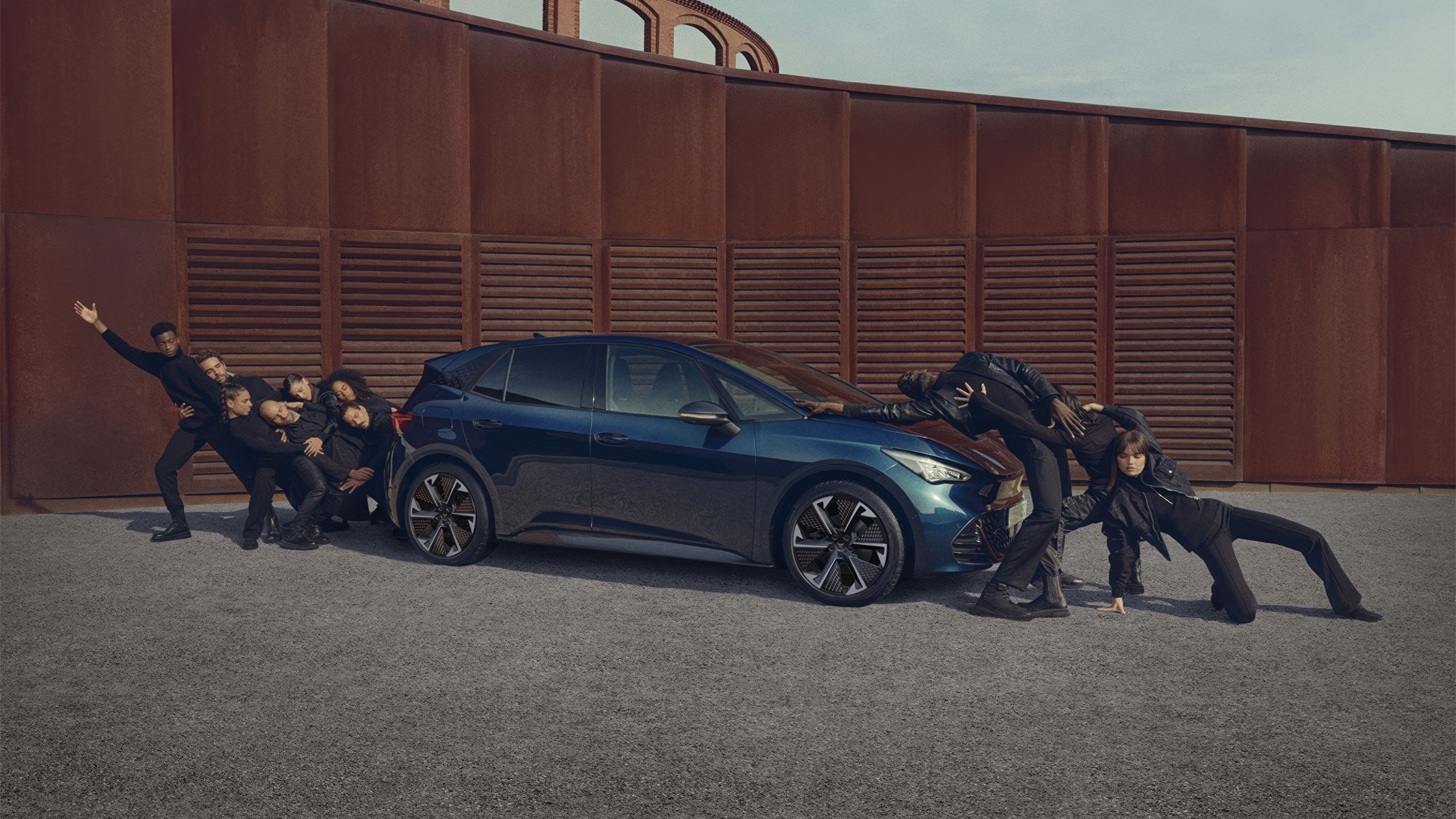 CUPRA Born in Aurora Bklue with 20 inch Thunderstrom aero rims with people posing infront and behind the car.